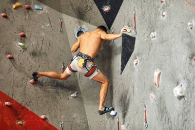 Erkek tırmanışçı spor salonunda egzersiz yapıyor, yapay duvara tırmanırken kayalar kullanıyor..