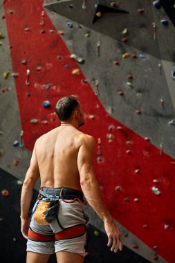 Duvarın yanında duran, kaya tırmanışına hazır bir sporcunun arkası..