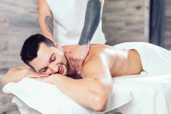 Joven hombre positivo disfrutando de recibir masaje en el centro de spa —  Fotos de Stock