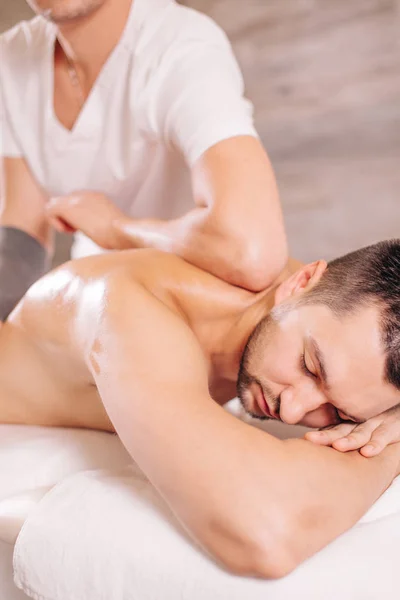 Людина з закритими очима лежить на ліжку і отримує масаж від болю назад — стокове фото