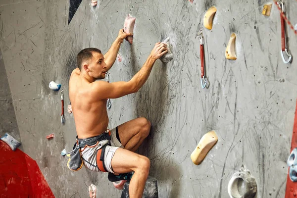 Homme grimpeur faisant de l'exercice dans la salle de gym, grimpant sur un mur artificiel avec des rochers. — Photo