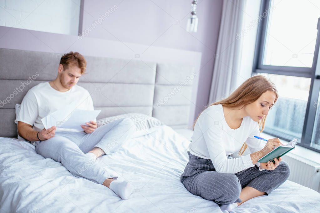 man is reading something while his girlfriend is writing in the diary