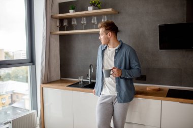 gelişigüzel bir kupa holding ve penceresine bakarak uykulu genç korku veren adam kılığında