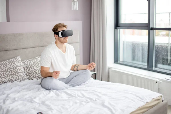 Homem bonito vestindo óculos de realidade virtual VR fazendo ioga em casa — Fotografia de Stock