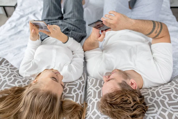 Dos personas agradables disfrutando de su tiempo mientras descansan en la cama con gadgets — Foto de Stock