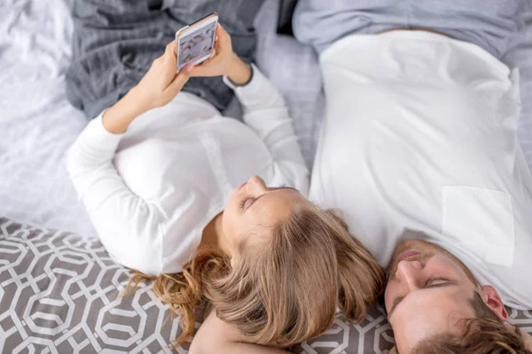 Esposa está sosteniendo el teléfono inteligente y acostado en la cama con su marido — Foto de Stock