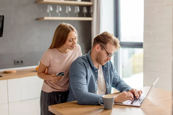 Lachende mooi meisje beheersing van haar echtgenoot werk op de laptop — Stockfoto