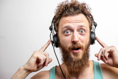 Kıvırcık saçlı ve sakallı beyaz adam kameraya şaşkın şaşkın bakıyor.