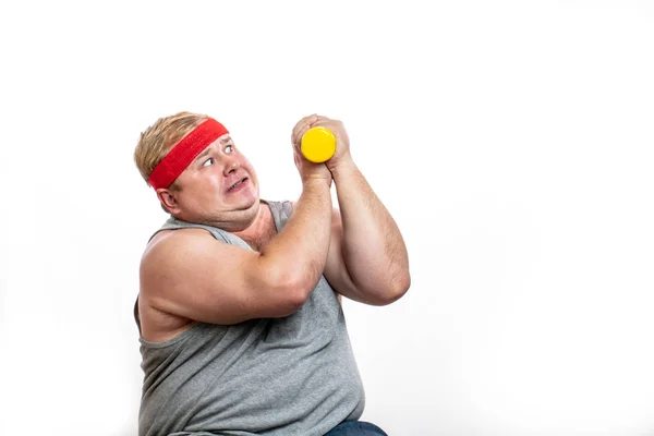 Gordo divertido hombre en rojo diadema muestra sus músculos con dummbell y emociones —  Fotos de Stock