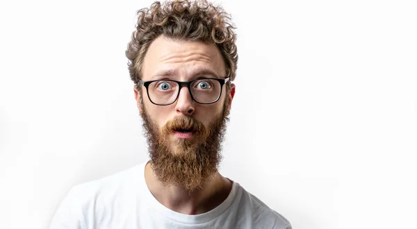Surprised caucasian man with curly hair and beard stares in amazement at camera — Stock Photo, Image