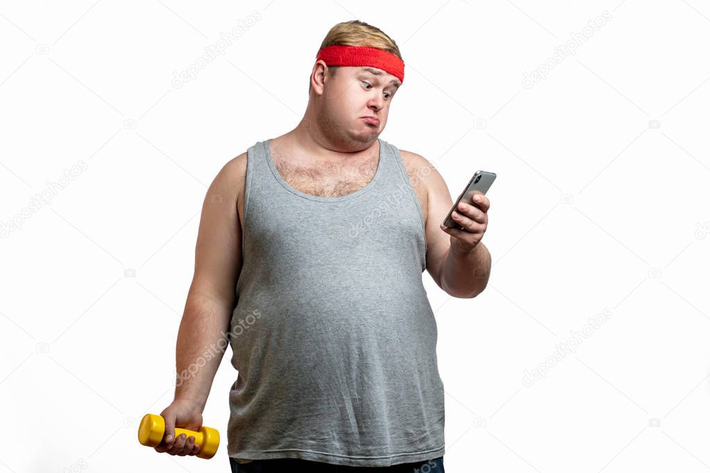 Waist-up shot of displeased gloomy obese male fatso in casual t-shirt, staring disappointed at camera, frowning and expressing dislike, looking at smartphone