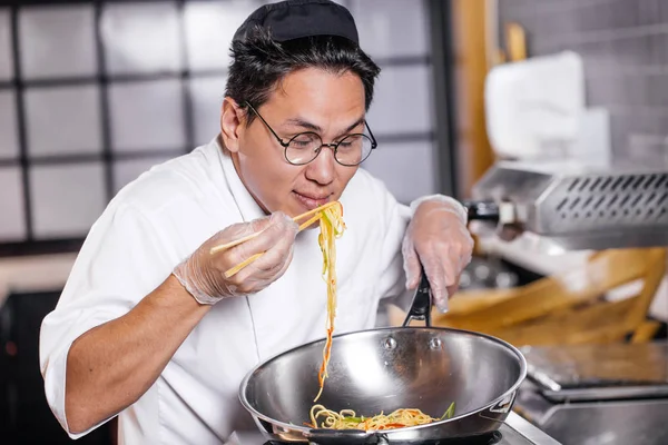 Aantrekkelijke Aziatische chef-kok genieten van het eten van noedels — Stockfoto