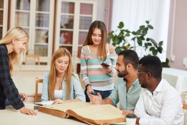 Çeşitli çok ırklı öğrenciler kütüphane büyük eski kitap ile boş zaman geçirmek