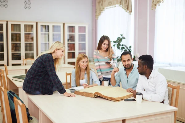 Diverse multiracial students spending leisure time in library with big old book