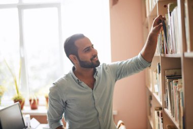 Genç Arap sakallı erkek öğrenci kitap kütüphane rafları arasında seçme