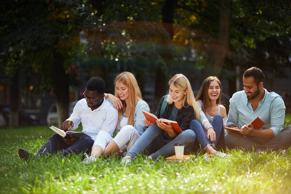 Mixed-race group of students sitting together on green lawn of university campus