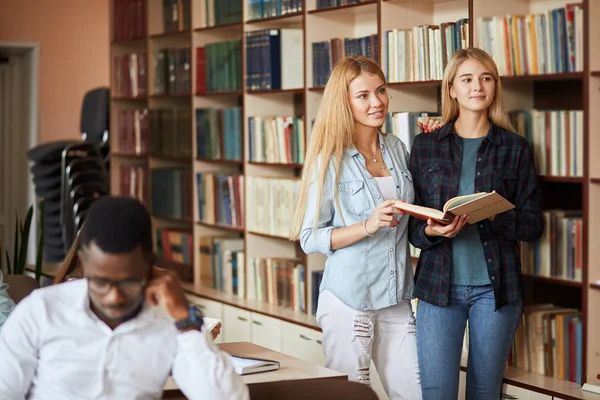 İki genç beyaz kız öğrencilerin kütüphanede kitap seçin — Stok fotoğraf