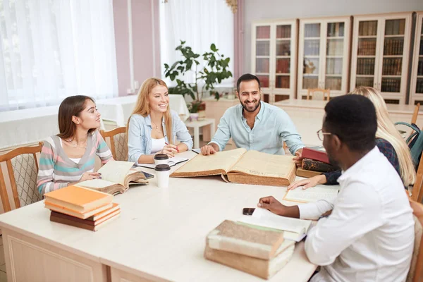 Group of multiracial people studying with books in college library.