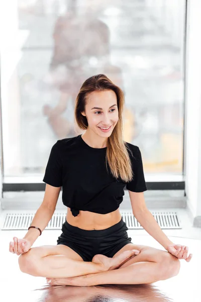 Cheerful girl in lotus posture sitting in front of the window — Stock Photo, Image