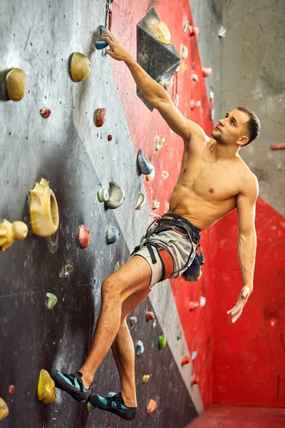 Man climber on artificial climbing wall in bouldering gym