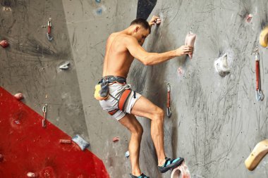 Erkek tırmanışçı spor salonunda egzersiz yapıyor, yapay duvara tırmanırken kayalar kullanıyor..