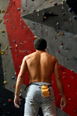 Duvarın yanında duran, kaya tırmanışına hazır bir sporcunun arkası..