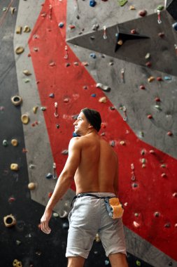 Duvarın yanında duran, kaya tırmanışına hazır bir sporcunun arkası..