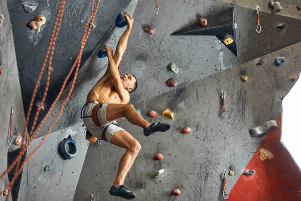 Homme grimpeur faisant de l'exercice dans la salle de gym, grimpant sur un mur artificiel avec des rochers. — Photo