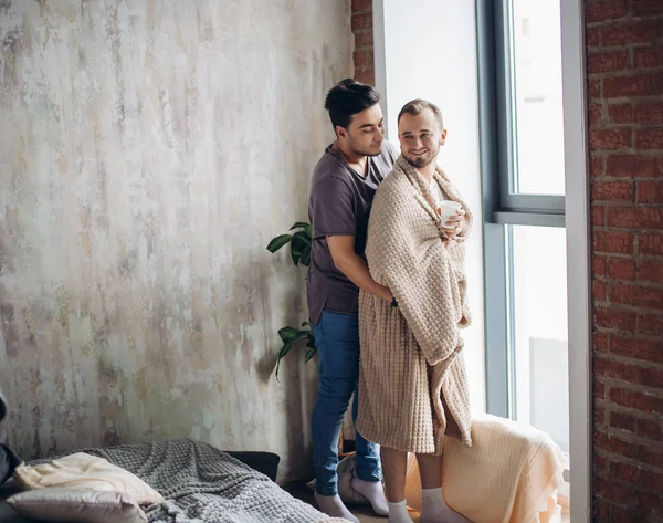 Two handsome homosexual guys while standing near window — Stock Photo, Image