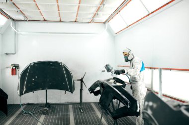 Özel garajda araba parçaları boyayan, kostüm ve koruyucu giysiler giyen işçiler.