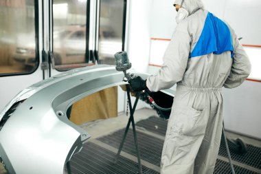 Özel garajda araba parçaları boyayan, kostüm ve koruyucu giysiler giyen işçiler.