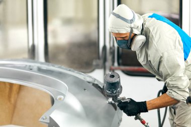 Özel garajda araba parçaları boyayan, kostüm ve koruyucu giysiler giyen işçiler.