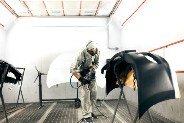 Özel garajda araba parçaları boyayan, kostüm ve koruyucu giysiler giyen işçiler.