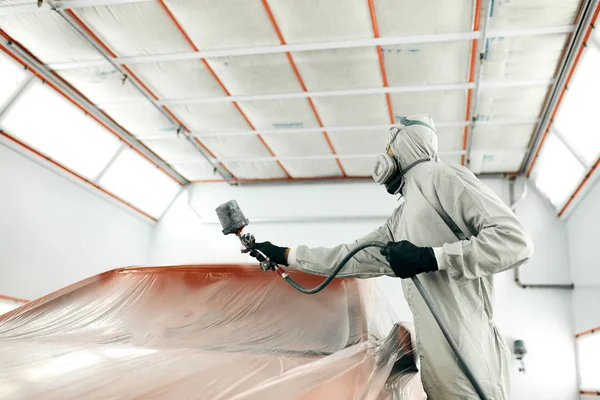 Auto malíř v ochranných pracovních oděvech a respirátor malování auto tělo v lakovací komoře — Stock fotografie