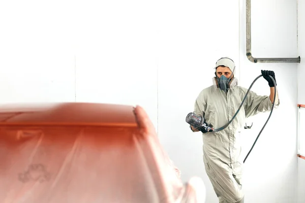 Auto målare i skyddsarbetskläder och respirator målning bil kropp i färg kammare — Stockfoto