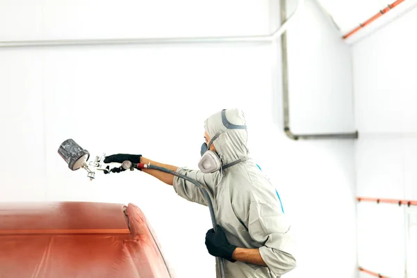 Auto pintor en ropa de trabajo protectora y respirador pintura carrocería del coche en la cámara de pintura — Foto de Stock