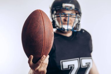 Koruyucu üniformalı ve kasklı Amerikan futbolcusu elinde top tutuyor.