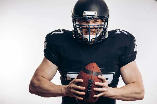 Joueur de football américain musclé en uniforme de protection et casque tenant le ballon — Photo