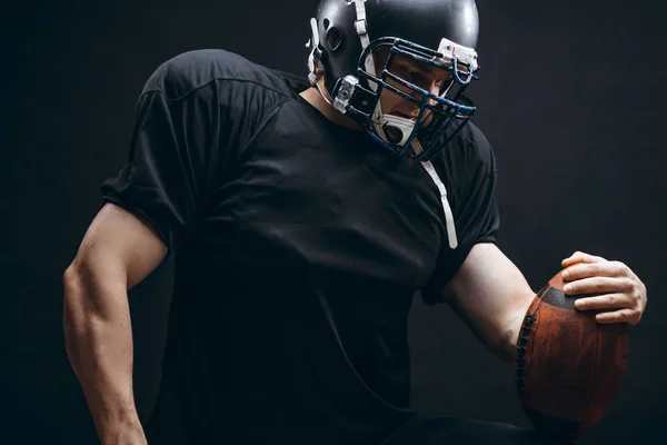 Αμερικανός ποδοσφαιριστής σε μαύρο αθλητικό ένδυμα με μπάλα σε μαύρο φόντο — Φωτογραφία Αρχείου