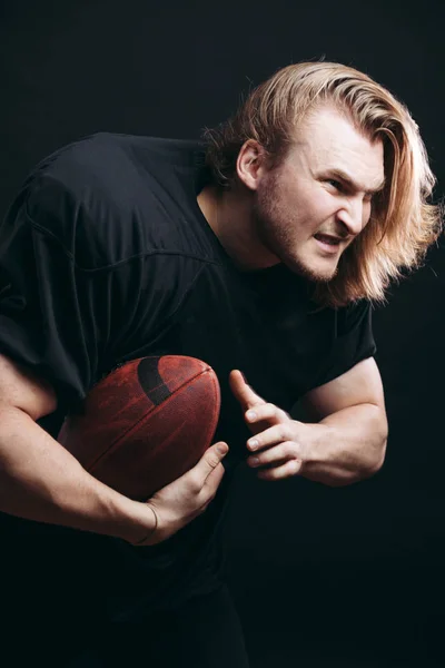 Entschlossener American-Football-Spieler in Aktion isoliert auf schwarzem Hintergrund — Stockfoto