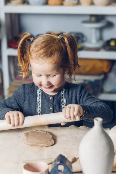 Mignonne fille impressionnante en utilisant un rouleau à pâtisserie pendant la leçon d'art — Photo