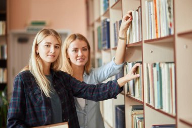 İki genç beyaz kız öğrencilerin kütüphanede kitap seçin