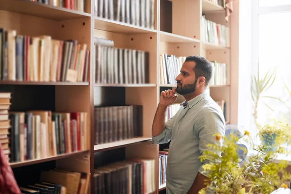 Young Arabian bearded male student choosing book between shelves in the library