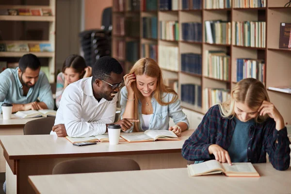 Grupo de estudantes felizes lendo livros e se preparando para exame na biblioteca — Fotografia de Stock