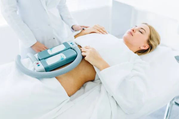 Mujer joven acostada en el sofá médico con elementos de refrigeración en el vientre en la clínica —  Fotos de Stock