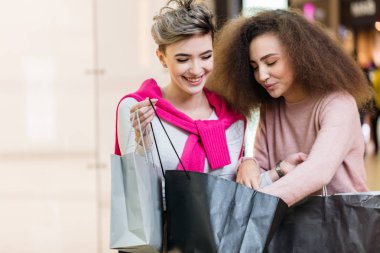 Esmer ve sarışın alışveriş torbalarına bakıyorlar, alışverişleri tartışıyorlar..