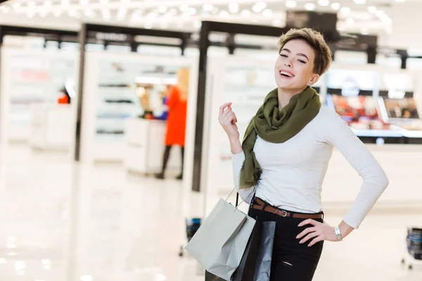 Glimlachende vrouw draagt een aantal boodschappentassen met winkels op de achtergrond — Stockfoto