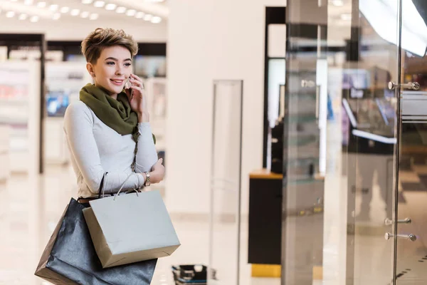 Vrouw met boodschappentassen, met behulp van een smartphone tijdens het winkelen in het winkelcentrum — Stockfoto