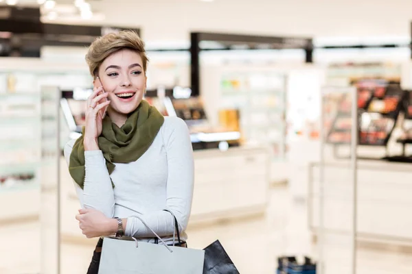 Vrouw met boodschappentassen, met behulp van een smartphone tijdens het winkelen in het winkelcentrum — Stockfoto