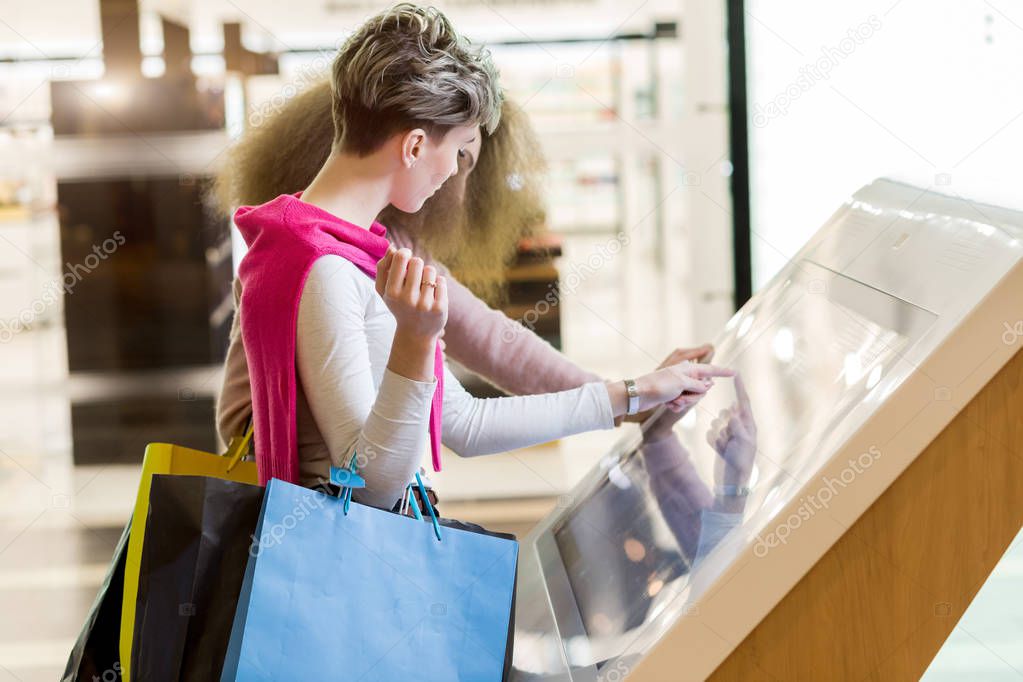 Two girlfriends looking at information board with map of mall while shopping.